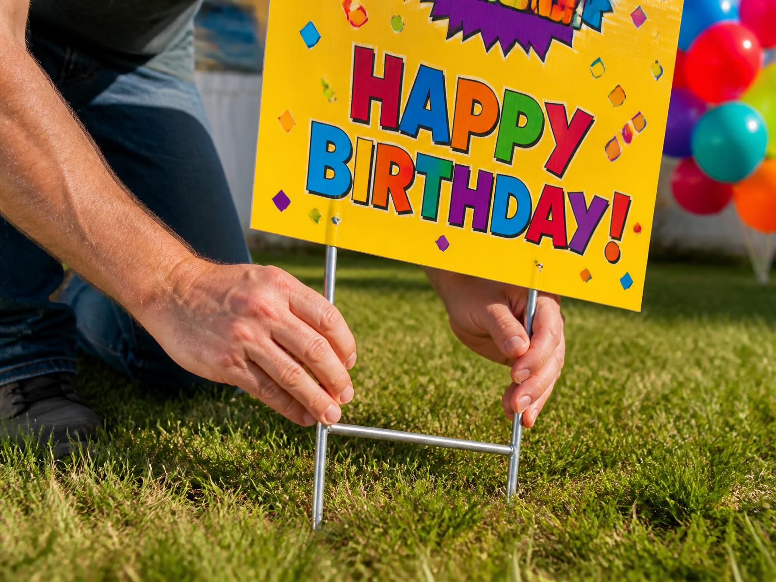 bright birthday yard sign staked in grass beside balloons in warm afternoon light