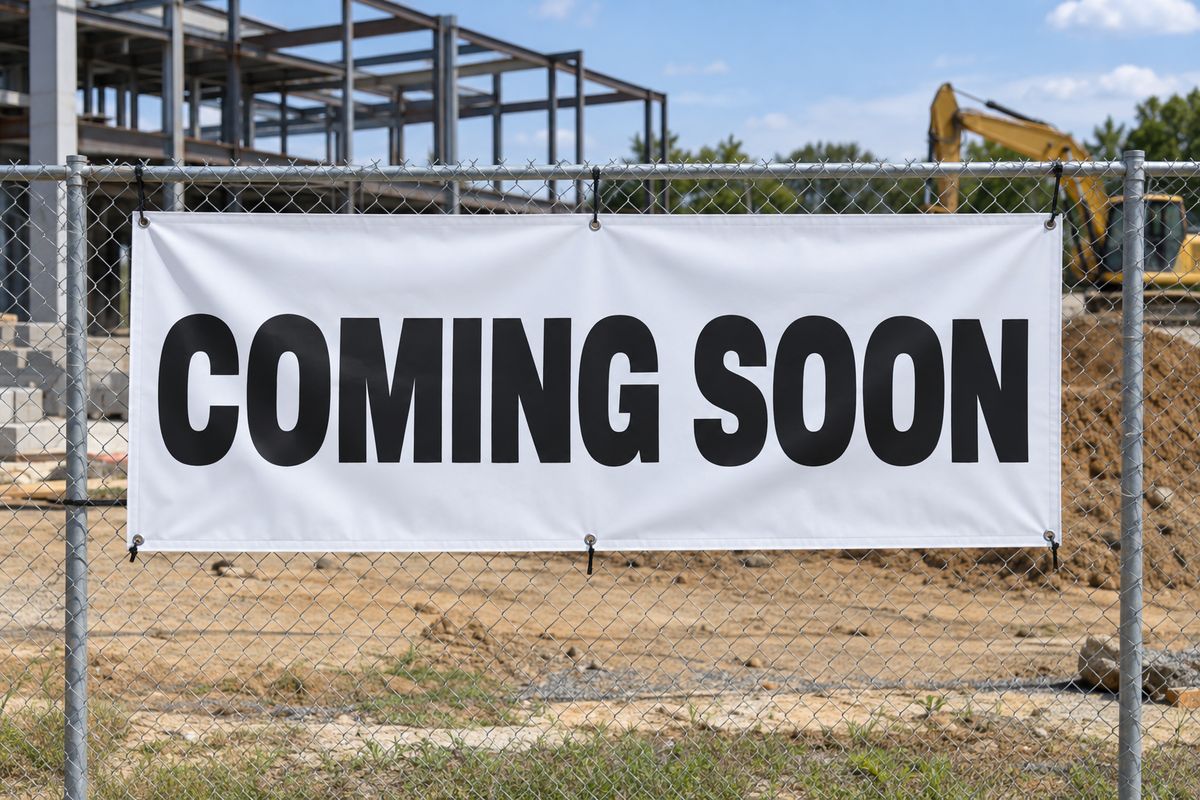 A Coming Soon vinyl banner on a construction site fence.