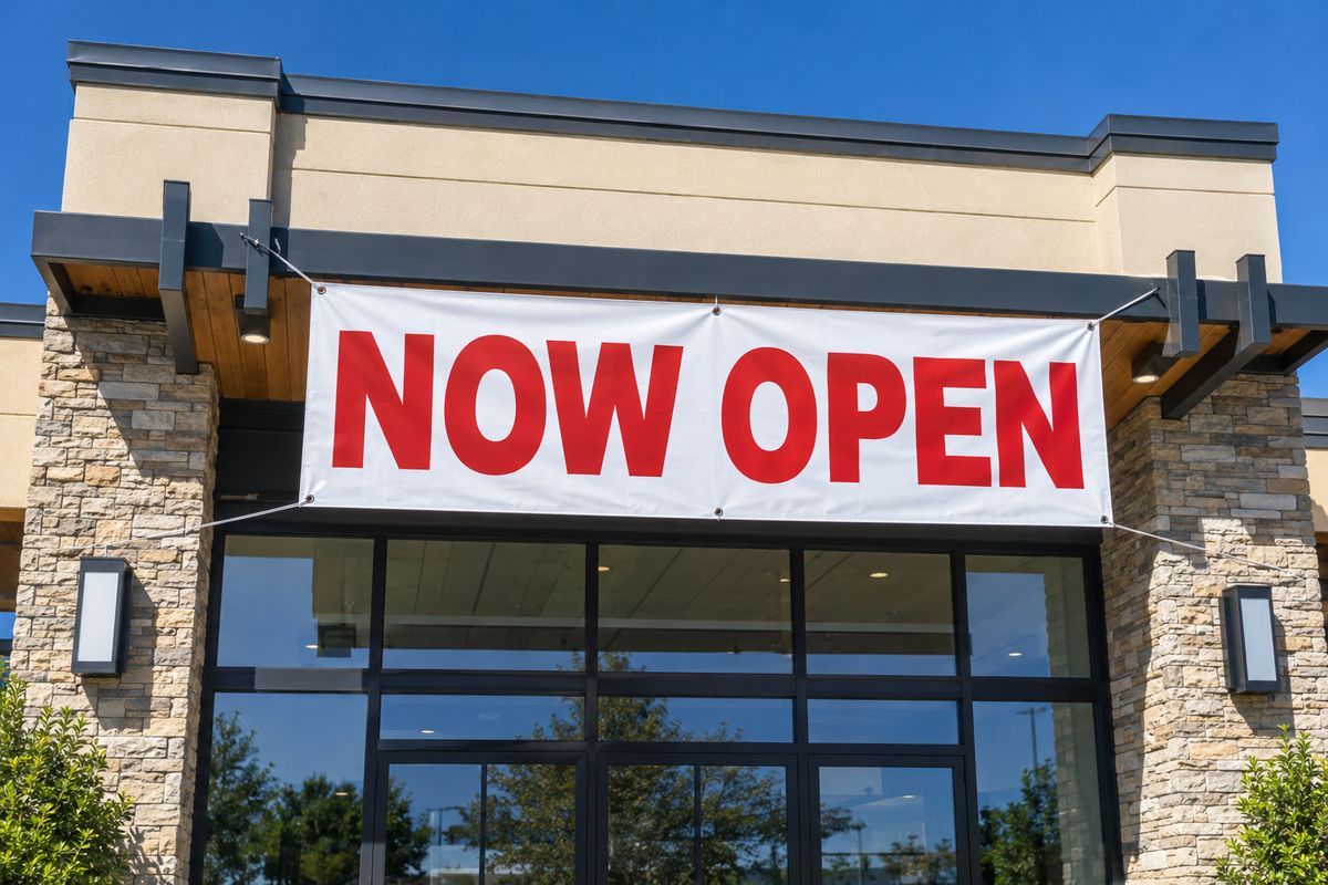 A Now Open vinyl banner on a building in bright sun.