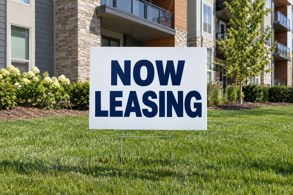 A Now Leasing yard sign on a modern apartment building lawn.