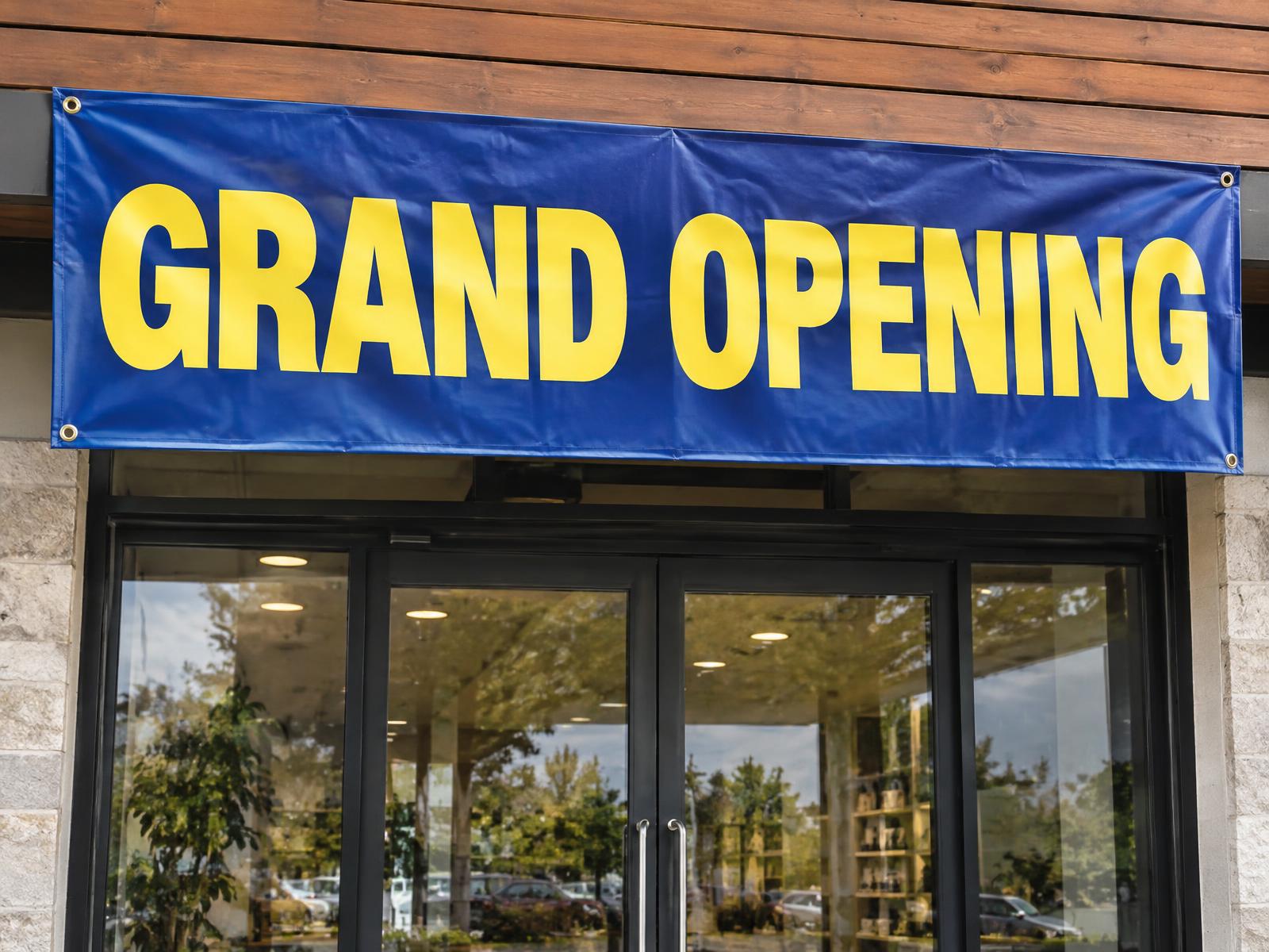 3 x 6 ft Grand Opening vinyl banner in yellow on navy above a small shop entrance